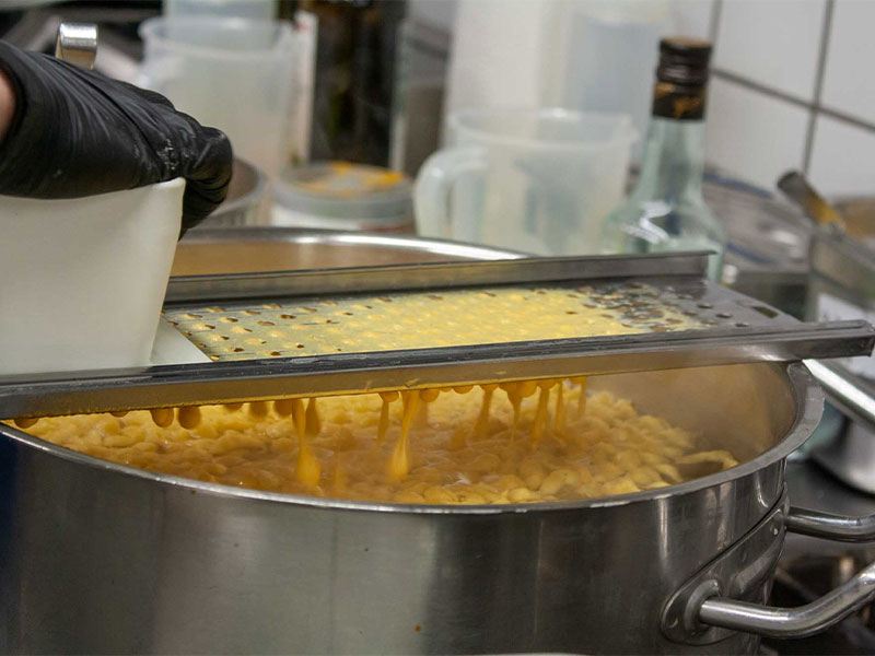 Zubereitung von frischen Spätzle in einer Küche mit Spätzlehobel und Kochtopf