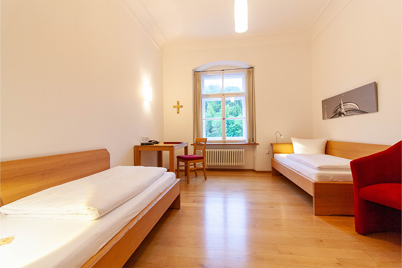 Zimmer mit zwei Einzelbetten und ein roten Hocker im Gästehaus St.Georg