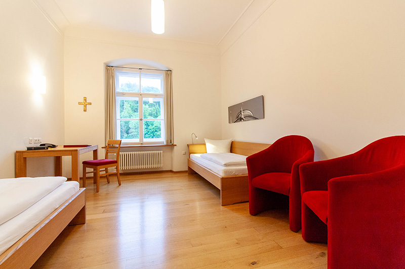 Zimmer mit zwei Einzelbetten und zwei roten Hockern im Gästehaus St.Georg